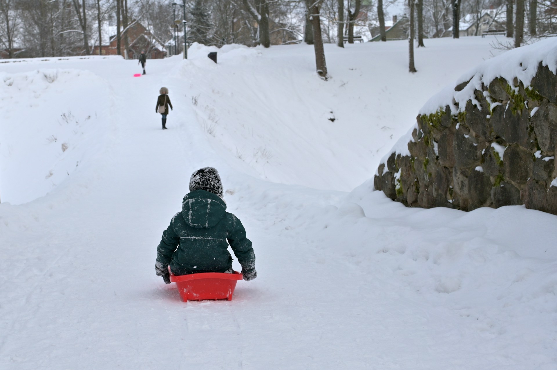Barn som åker i en röd pulka nedför en snöklädd backe