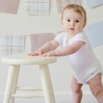 Bild på ett barn som står upp med hjälp av en pall som stöd.