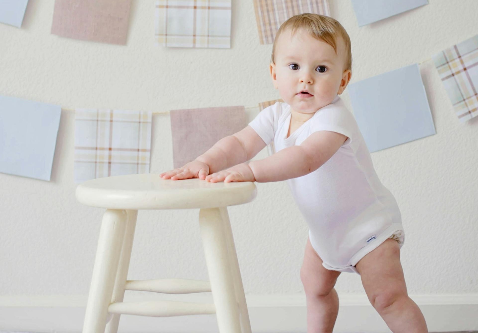 Bild på ett barn som står upp med hjälp av en pall som stöd.