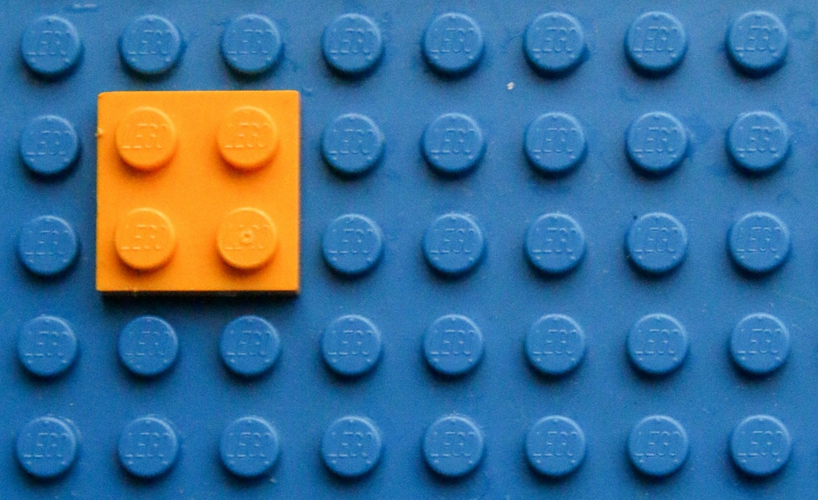 En liten orange fyrkantig legobit på en stor blå legobit.