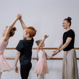 Tre barn som dansar balett med en vuxen bredvid sig.