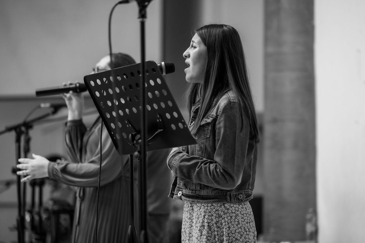 En svartvit bild på två personer som står och sjunger i varsinn mikrofon.