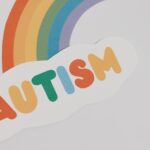 En regnbåge och ett moln skrivet autism i regnbågens färger