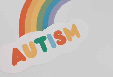 En regnbåge och ett moln skrivet autism i regnbågens färger