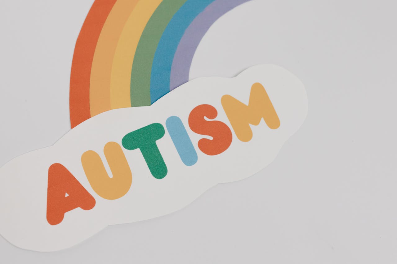 En regnbåge och ett moln skrivet autism i regnbågens färger