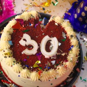 Bild på en tårta som det står "30" på. Tårtan står på ett bord med dekorationer och partyhattar.