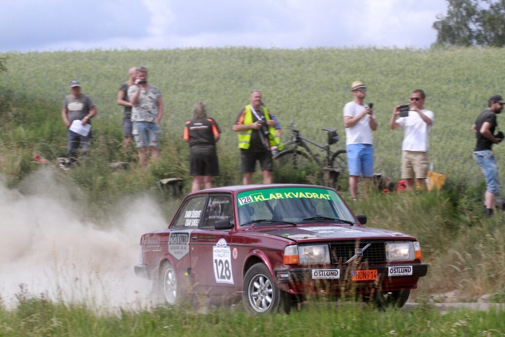 Rallybil i fart med åskådare i bakgrunden.