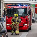 Brandmän i utrustning står framför brandbilar på en stadsgata, redo för räddningsinsats.
