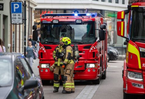 Brandmän i utrustning står framför brandbilar på en stadsgata, redo för räddningsinsats.