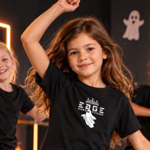 Två flickor och en pojke i svarta T-shirts som dansar i en mörk halloweenutsmyckad danslokal . T-shirten på flickan i mitten har ett vitt tryck där det står "Edge dance studios" och ett spöke.