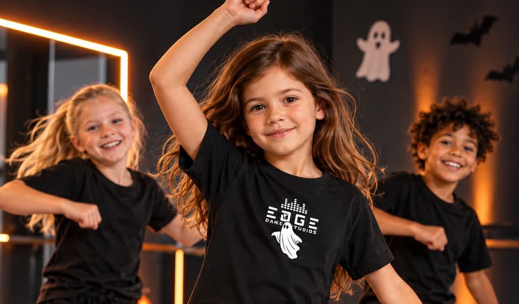 Två flickor och en pojke i svarta T-shirts som dansar i en mörk halloweenutsmyckad danslokal . T-shirten på flickan i mitten har ett vitt tryck där det står "Edge dance studios" och ett spöke.