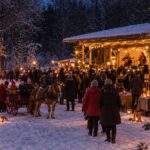 Julmarknad i vinterlandskap. En julpyntad dansbana på höger sida med två kvinnor som spelar musik. Försäljningsstånd, människor som går runt, barn som åker häst och vagn, en eldshow, eldkorg och marschaller.
