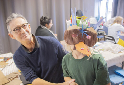 Bild på en vuxen som sitter bredvid ett barn som har en mask på sig.