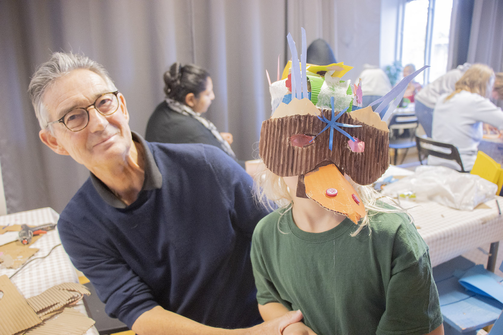 Bild på en vuxen som sitter bredvid ett barn som har en mask på sig.