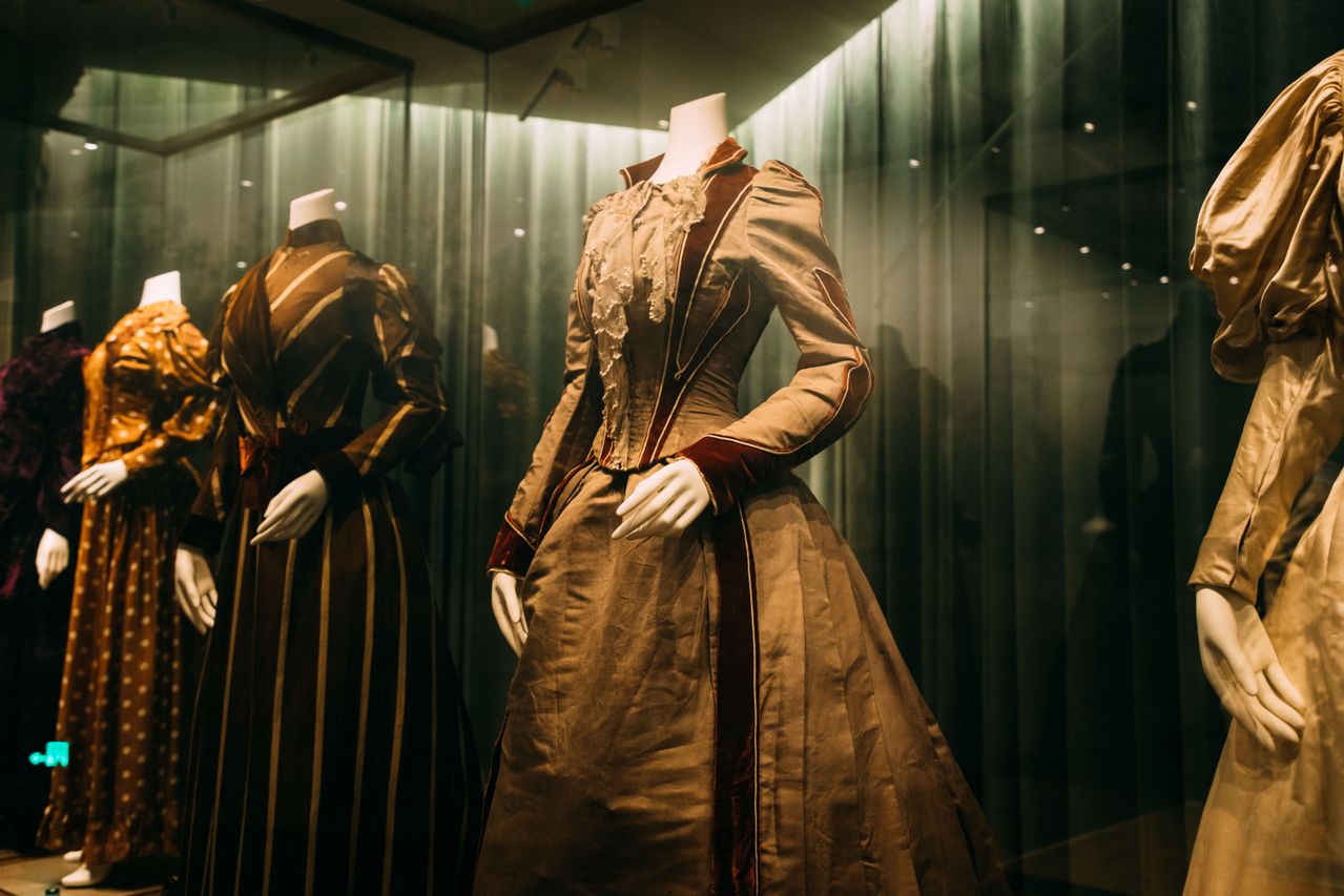 Eleganta vintageklänningar på modeller visade i en museiutställning.